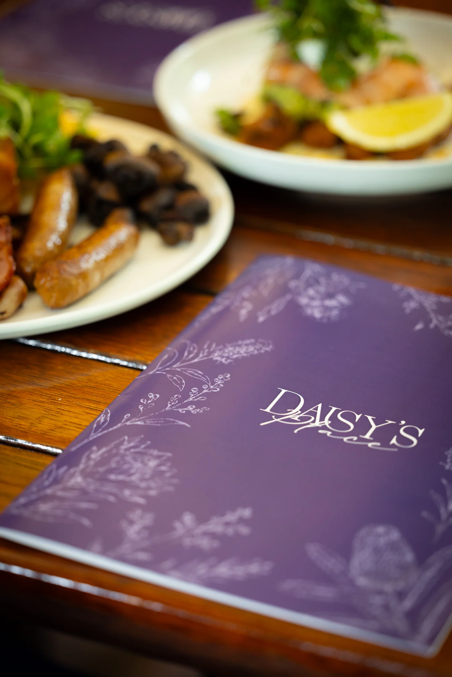 Daisy’s Place purple botanical menu beside breakfast dishes on a timber table