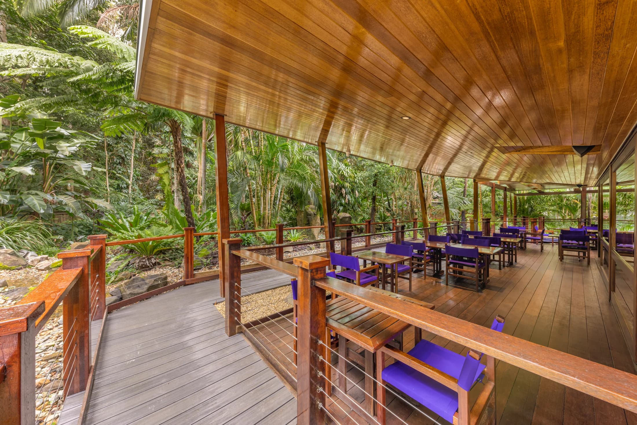 Daisy’s Place covered timber dining terrace with purple chairs beside the rainforest garden.
